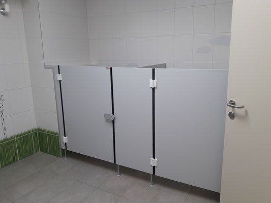 Eine leere Toilette mit weißen Fliesenwänden, grauen Trennwänden und einem silbernen Türgriff.