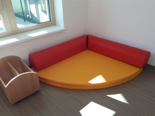 Eine rote und gelbe Eckbank mit einer Holzaufbewahrungsbox auf einem Boden mit einer weißen Wand und einem Fenster.