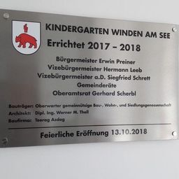 Eine Plakette für den Kindergarten Winden am See, errichtet 2017-2018. Sie listet Offizielle auf, darunter Bürgermeister Erwin Preiner, Vizebürgermeister Hermann Leeb und andere. Der Architekt ist Dipl. Ing. Werner M. Thell. Die feierliche Eröffnung war am 13.10.2018.