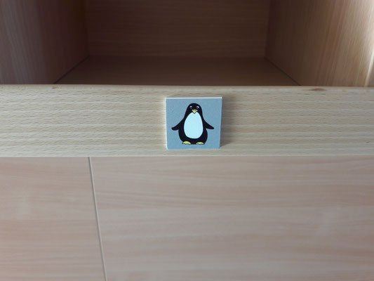 Eine kleine quadratische Holzschublade mit einem Pinguin-Aufkleber auf der Vorderseite. Die Schublade ist geschlossen und es gibt einen kleinen offenen Raum darüber.