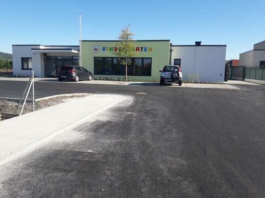 Ein neues Kindergartengebäude ist zu sehen, vor dem zwei Autos geparkt sind. Das Gebäude ist grün und weiß.
