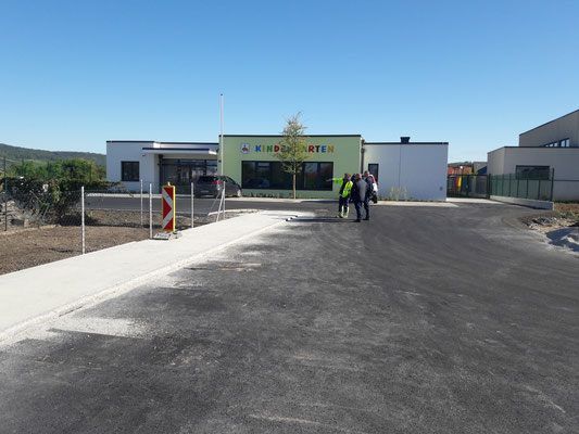 Ein Gebäude mit dem Schild Kindergärten steht vor einer Straße mit drei Menschen, die gehen.
