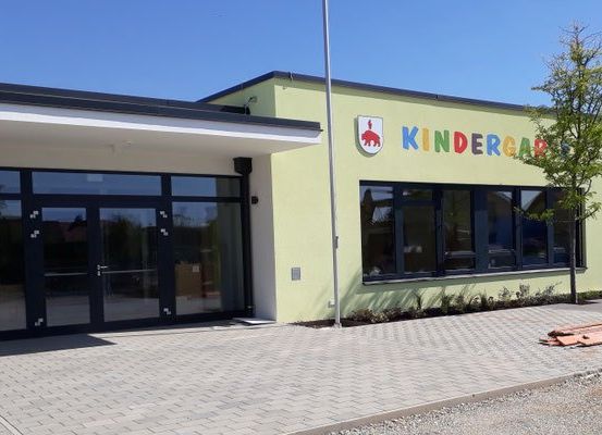 Das Äußere eines Gebäudes mit dem Wort Kindercar in bunten Buchstaben über dem Eingang und großen Glastüren.