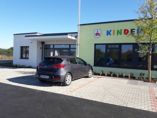 Ein silbernes Auto steht vor einem Gebäude mit Glasfenstern und einem Schild, auf dem Kinder steht.