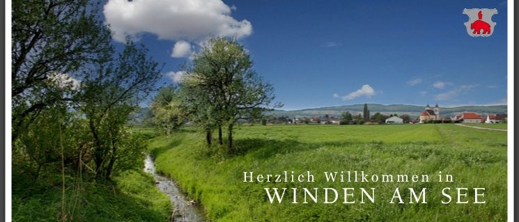 Ein herzliches Willkommen in Winden am See mit Blick auf eine friedliche Landschaft, einen kleinen Bach und ein reizendes Dorf im Hintergrund.