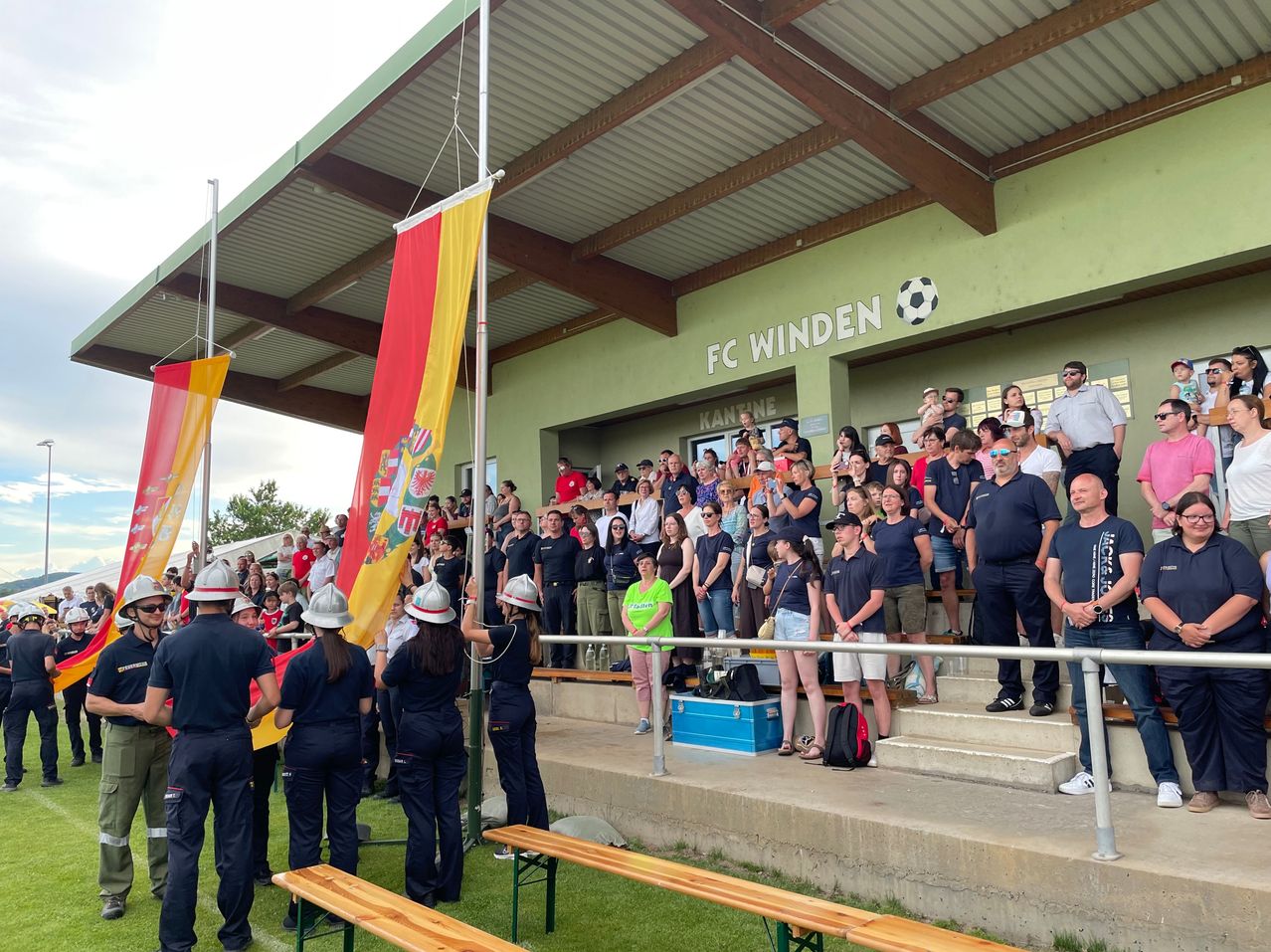 A group of people, likely fans, are standing on the stairs of a stadium. They are wearing uniforms, hats, and shoes. Some are holding flags, while others are watching the game.