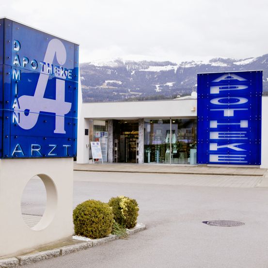 Ein Apothekenschild ist vor einem Gebäude mit einem verschneiten Berg im Hintergrund angebracht.