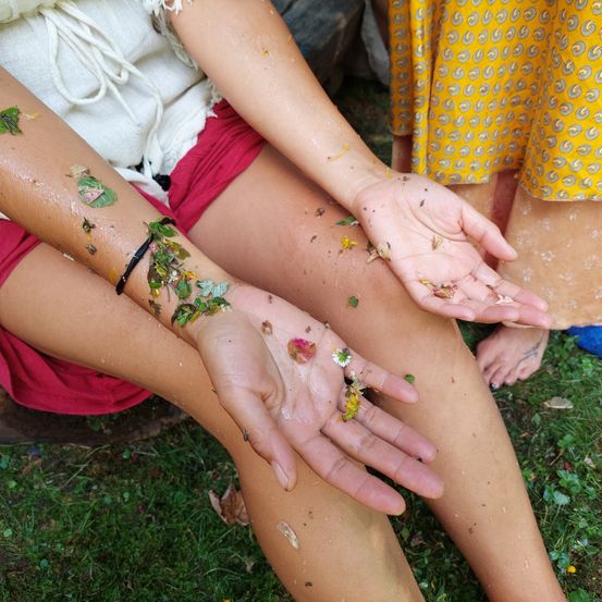 Eine Person mit Blättern und Schmutz an Beinen und Händen sitzt auf Gras mit einer weiteren Person dahinter.