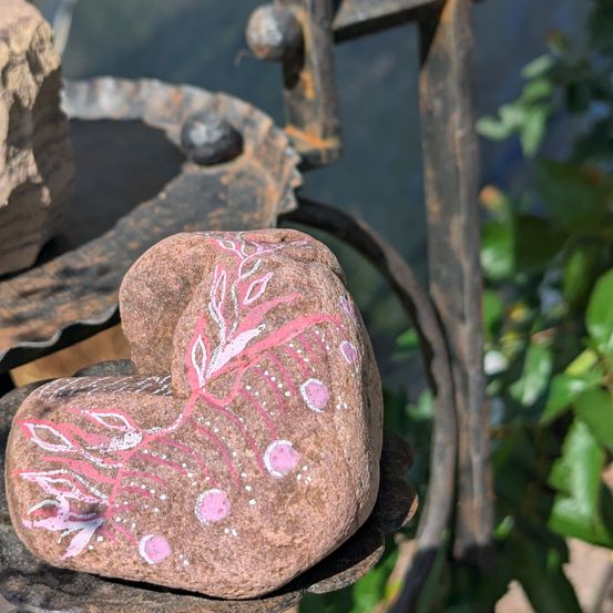 Ein herzförmiger Stein mit rosa Blumendesigns ruht auf einem rustikalen Metallständer, umgeben von Grün.