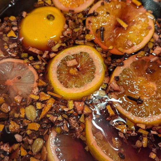 Ein Nahaufnahme von einem köchelnden Topf, gefüllt mit einer Mischung aus Zutaten, einschließlich geschnittenen Grapefruits, Zitronen und Gewürzen, die in einer Flüssigkeit eingetaucht sind.