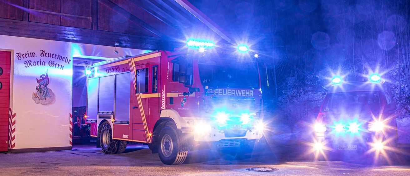 Ein roter Feuerwehrwagen mit blauen Lichtern steht nachts vor einer Feuerwache.