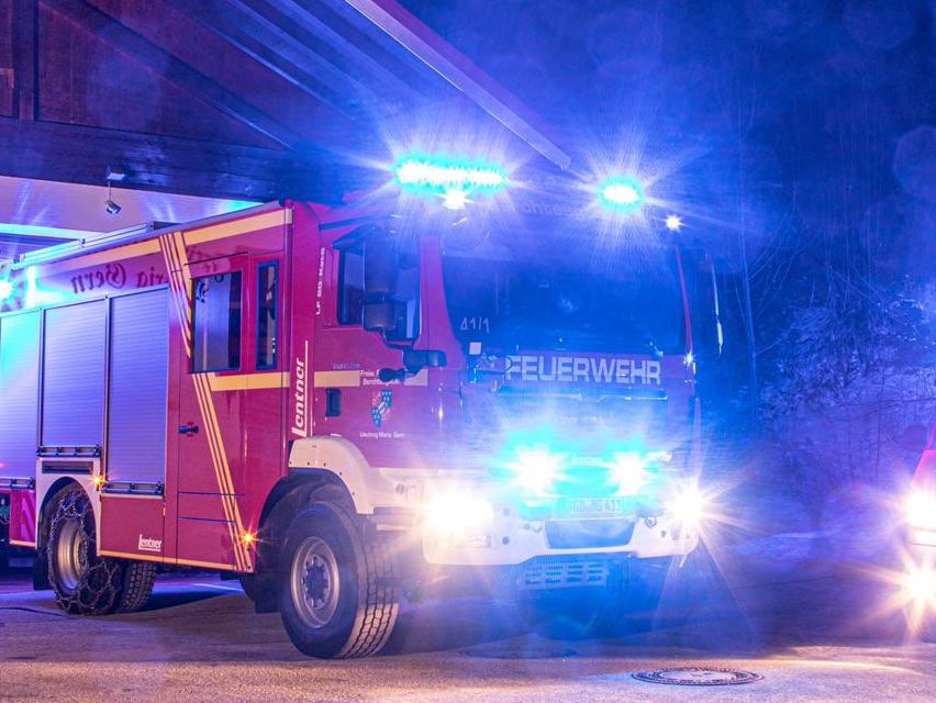 Ein roter Feuerwehrwagen mit blauen Lichtern steht nachts vor einer Feuerwache.