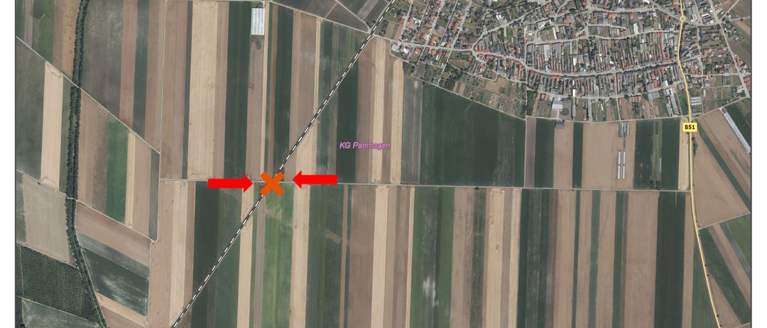 Eine Luftaufnahme eines ländlichen Gebiets mit Feldern und Gebäuden. Das Feld hat ein rotes X-Markierung und rote Pfeile, die darauf zeigen. Das Gebiet hat ein Rastermuster.