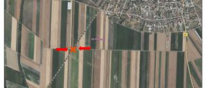 Eine Luftaufnahme eines ländlichen Gebiets mit Feldern und Gebäuden. Das Feld hat ein rotes X-Markierung und rote Pfeile, die darauf zeigen. Das Gebiet hat ein Rastermuster.