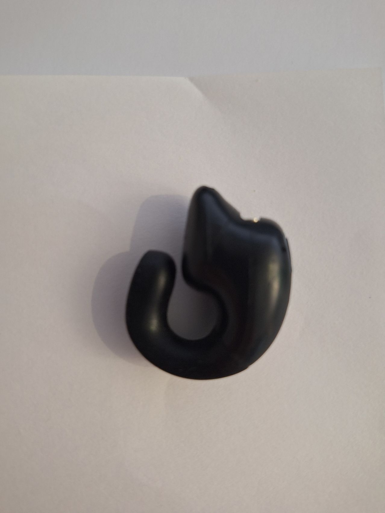 Ein schwarzer Gummihaken, möglicherweise Teil eines Kabelmanagementsystems, wird auf einem weißen Hintergrund gezeigt.