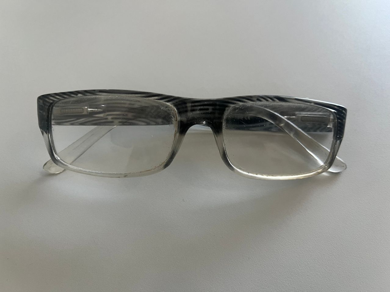 Ein Paar Brille mit klaren Rahmen und schwarz-weißen Zebra-ähnlichen Mustern an den Seiten. Die Gläser sind transparent und sauber.