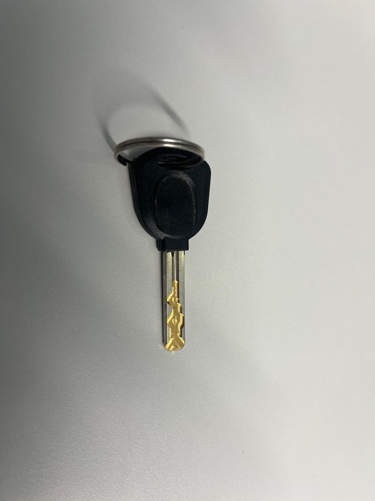 Ein schwarzer Autoschlüssel mit einer goldfarbenen Klinge ist an einem silbernen Schlüsselring befestigt und hängt an einer weißen Wand.