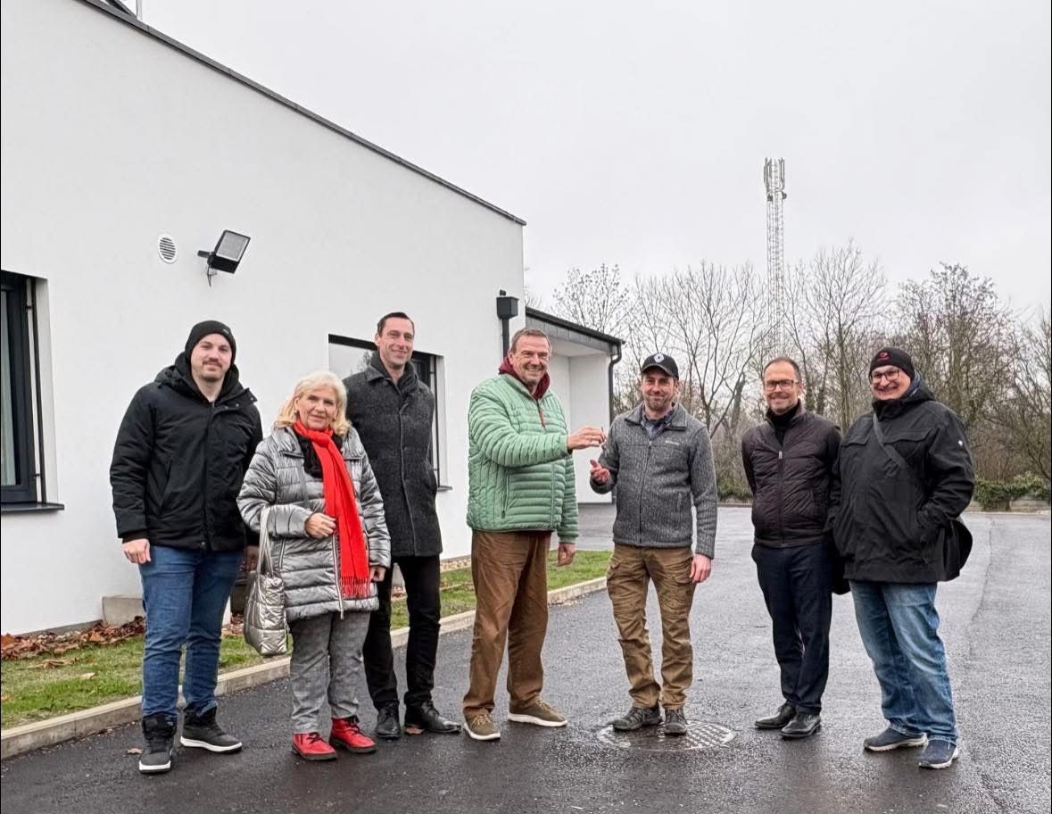 Eine Gruppe von Menschen in Winterkleidung steht vor einem Gebäude. Die Frau in der Mitte trägt einen roten Schal.