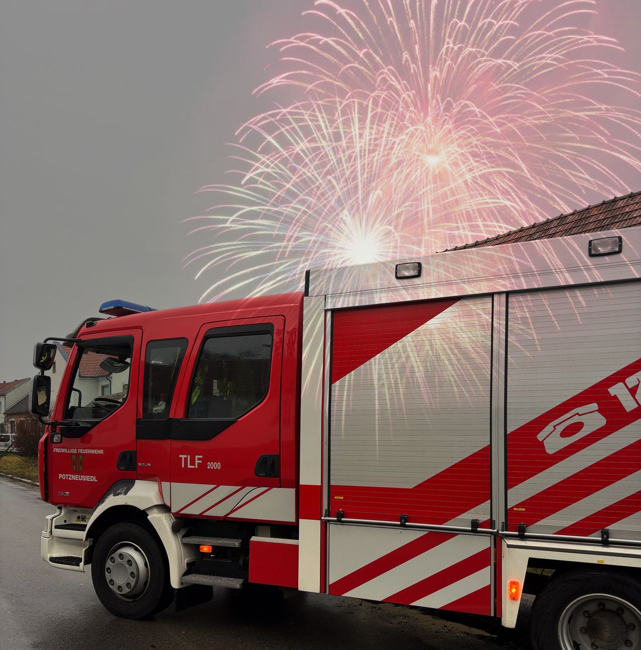 Ein Feuerwehrwagen mit der Nummer 2000 steht auf der Straße, während in der Luft Feuerwerke explodieren.