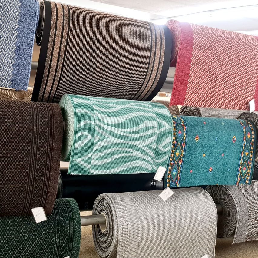 Eine Vielzahl von gerollten Teppichen wird in einem Geschäft ausgestellt, mit verschiedenen Farben und Mustern, darunter Blau, Braun, Rot und Grün.