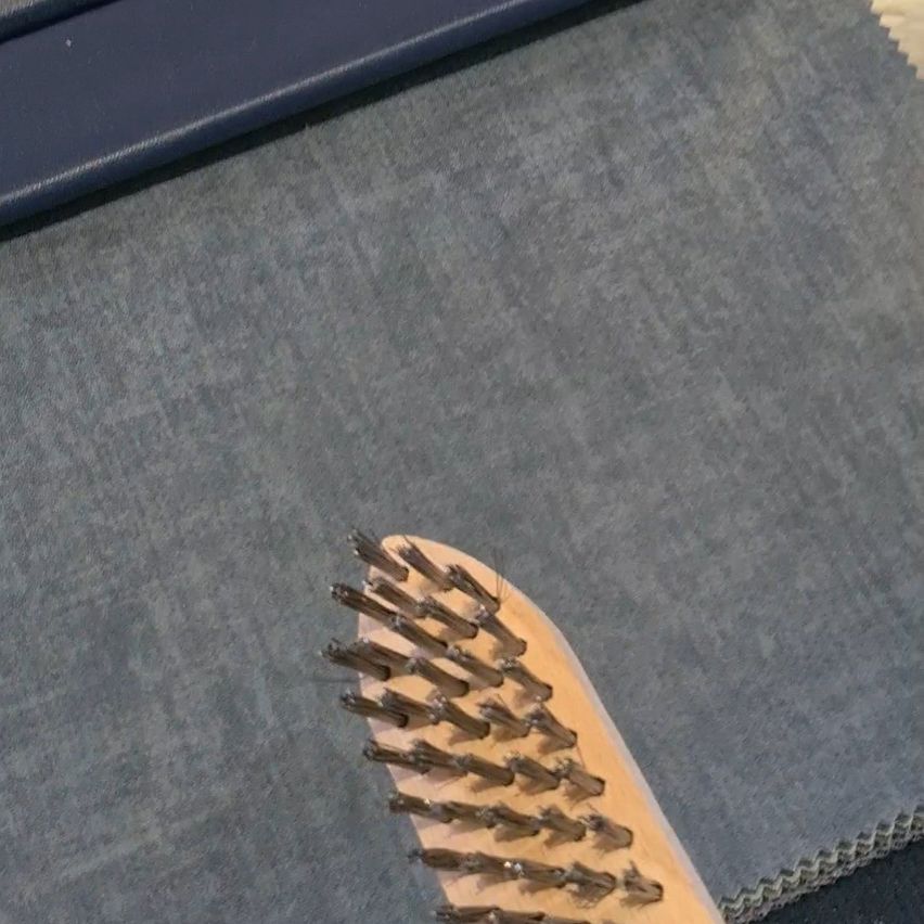 Eine Nahaufnahme eines Holzpinsels mit Borsten, der auf einer grauen Oberfläche, möglicherweise einem Teppich oder einer Matte, ruht.