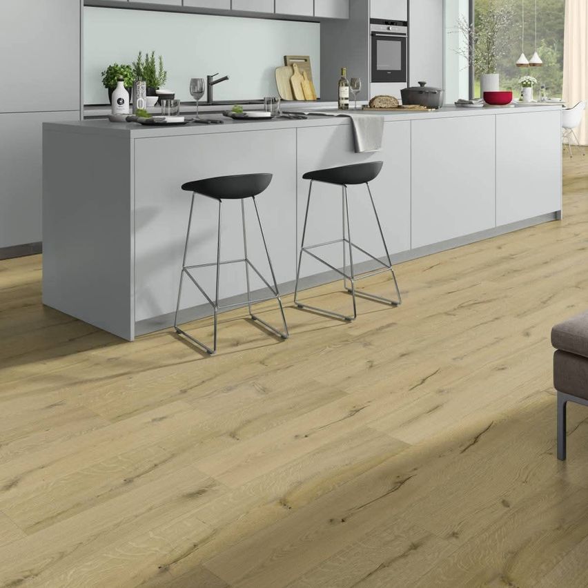 Eine moderne Küche mit hellen Holzböden, weißen Schränken und zwei schwarzen Barhockern. Eine Arbeitsplatte hat eine Schüssel, Teller, eine Flasche und ein Schneidebrett.