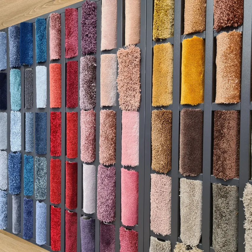 Eine Wand, die eine Reihe von Teppichmustern in verschiedenen Farben und Texturen in einem Rastermuster systematisch angeordnet zeigt.