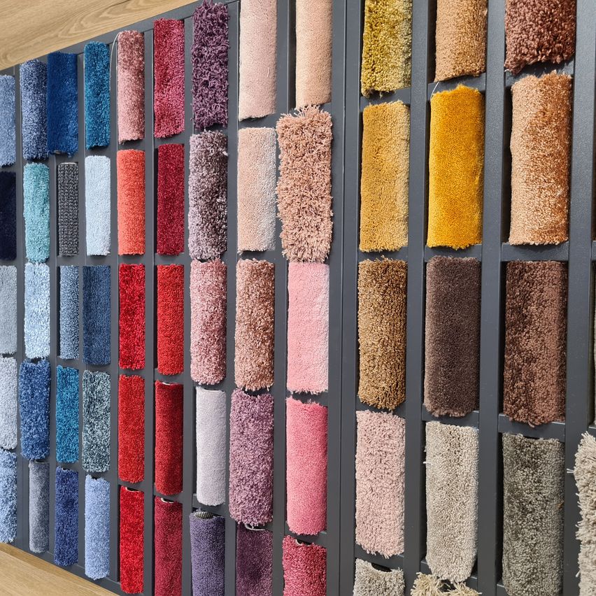 Eine Wand, die eine Reihe von Teppichmustern in verschiedenen Farben und Texturen in einem Rastermuster systematisch angeordnet zeigt.