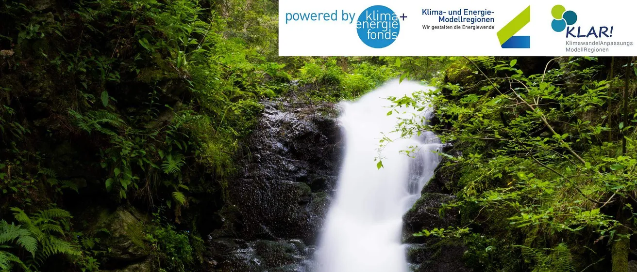 Ein Wasserfall stürzt an einem moosbewachsenen Felsen in einem dichten Wald hinab. Wassertropfen sprühen in die Luft. Oben ist 'Powered by Klimaenergiefonds' sichtbar.