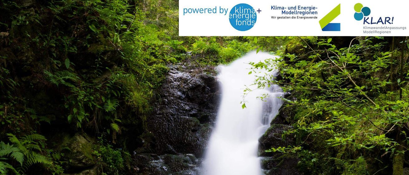 Ein Wasserfall stürzt an einem moosbewachsenen Felsen in einem dichten Wald hinab. Wassertropfen sprühen in die Luft. Oben ist 'Powered by Klimaenergiefonds' sichtbar.