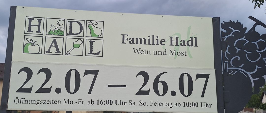 Ein Schild für Familie Hadl, einen Wein- und Apfelsaftproduzenten, mit Öffnungszeiten vom 22. bis 26. Juli.