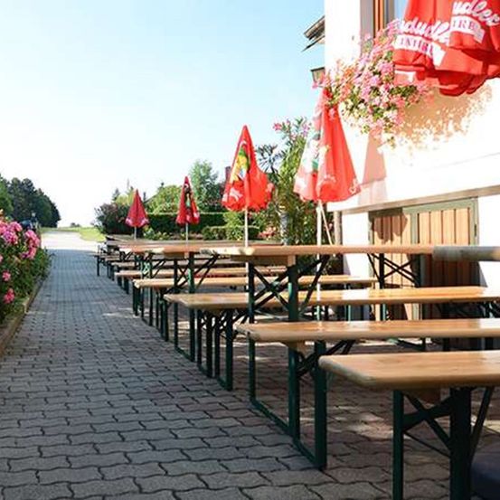 Eine Reihe von Holzbänken mit roten Schirmen und Blumen am Straßenrand.