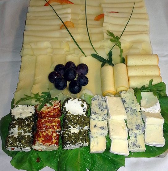 Ein Käsebrett mit verschiedenen Käsesorten und Trauben, auf grünen Salatblättern auf einer weißen Tischdecke angeordnet.