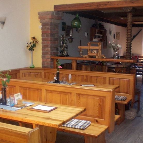 Ein rustikaler Holzspeisebereich mit Bänken, einer Theke und einer Ziegelwand. Vasen mit Blumen und Gegenständen auf der Theke. Ein Fenster sorgt für natürliches Licht.