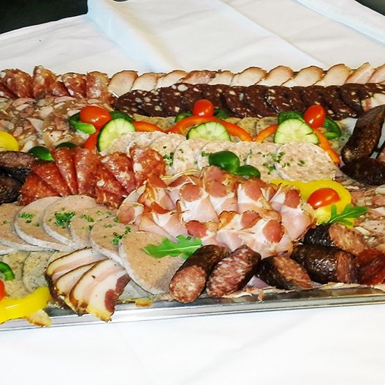 Ein Tablett gefüllt mit verschiedenen Arten von Wurst und Gemüse, einschließlich Tomaten, Gurken und Paprika, alles ordentlich auf einem weißen Tuch angeordnet.