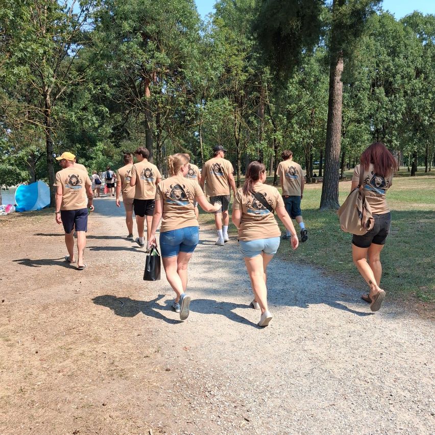 Eine Gruppe von Menschen in gleichen Shirts läuft auf einem Kiesweg in einem Park. Einige tragen Taschen, und der Weg ist von Bäumen umgeben.