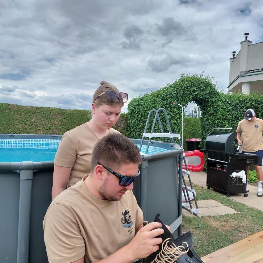 Two people are working on a project in a backyard with a pool and a grill in the background.