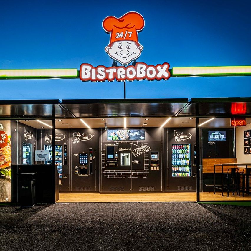Beleuchteter BistroBox 24/7-Kiosk bei Nacht mit Pizza-Werbung und Verkaufsautomaten.