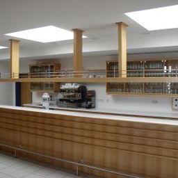 Ein Innenansicht einer modernen Bar mit einer hölzernen Theke, einer Kaffeemaschine und Regalen mit Gläsern unter Oberlichtern.