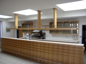 Ein Innenansicht einer modernen Bar mit einer hölzernen Theke, einer Kaffeemaschine und Regalen mit Gläsern unter Oberlichtern.