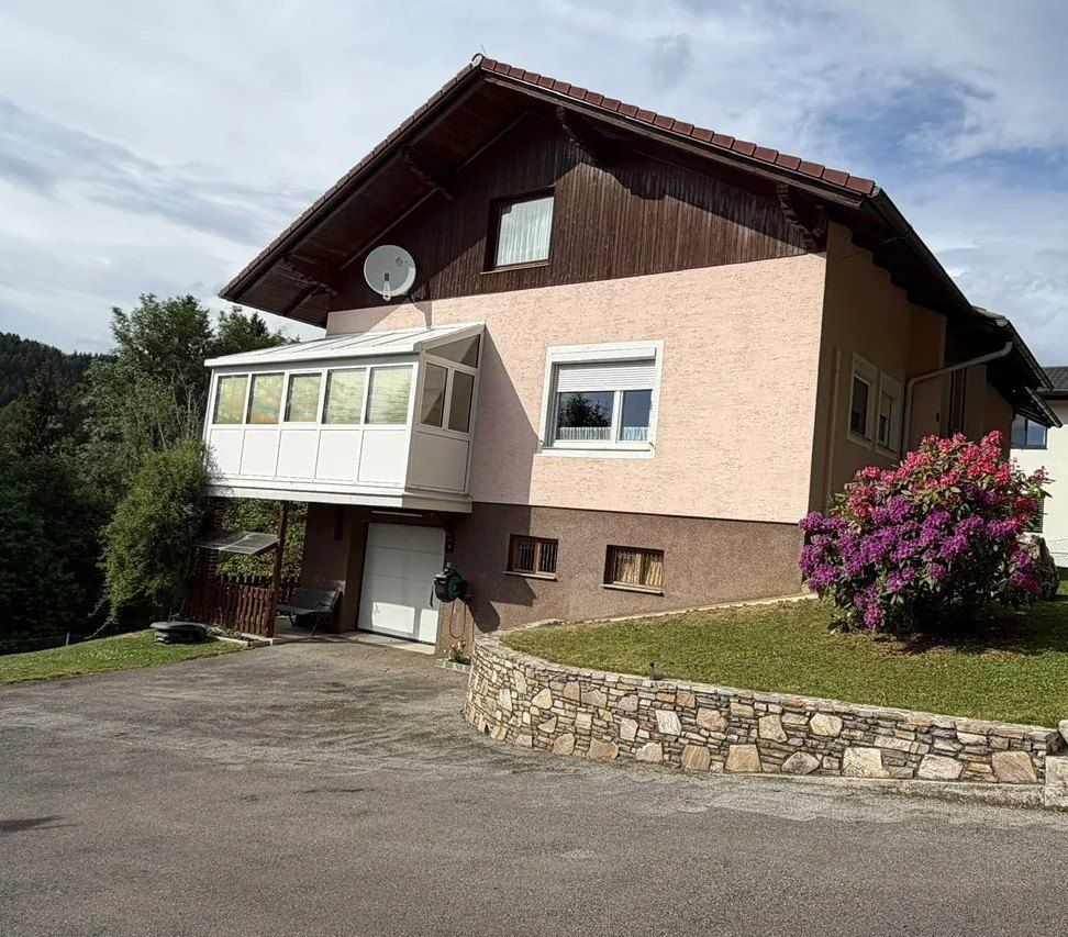 A two-story house with a brown roof, pink walls, and a white garage door. A satellite dish is mounted on the roof.