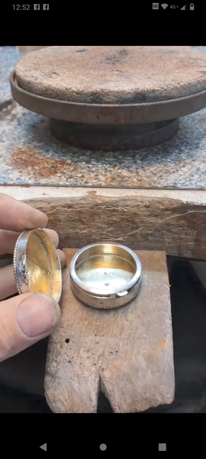 Eine Person hält eine silberne Taschenuhrenhülle und zeigt das Innenleben, mit einer polierten Metalloberfläche auf einem Holztisch.