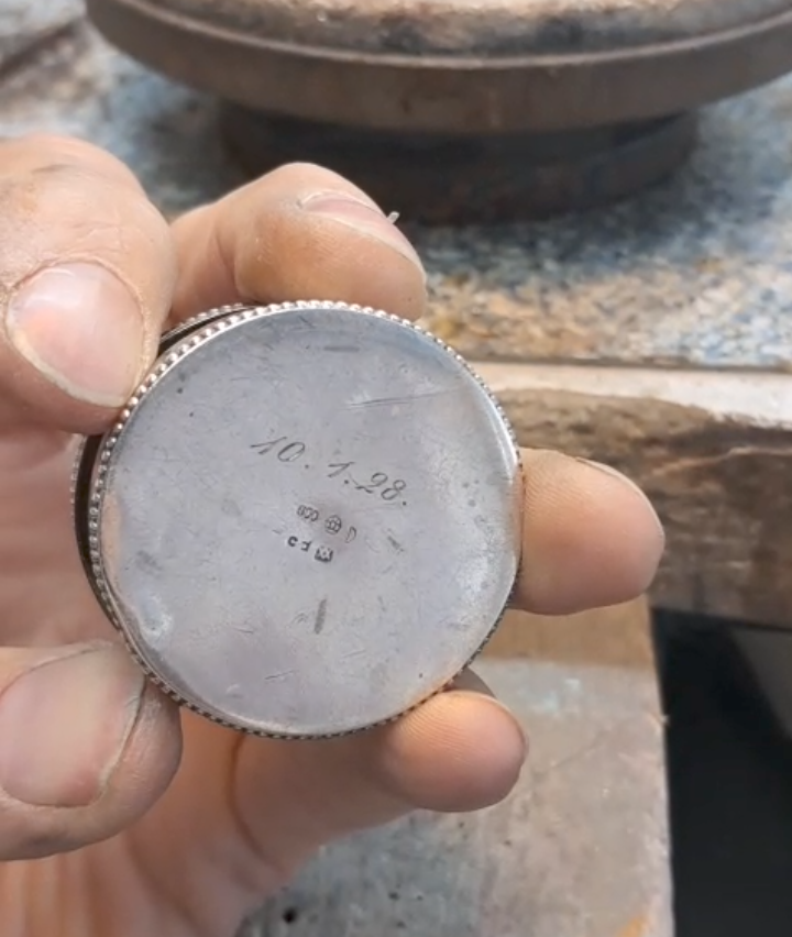 Eine Hand hält ein silbernes Vintage-Uhrengehäuse, das Zahlen und Text auf seiner Rückseite zeigt.