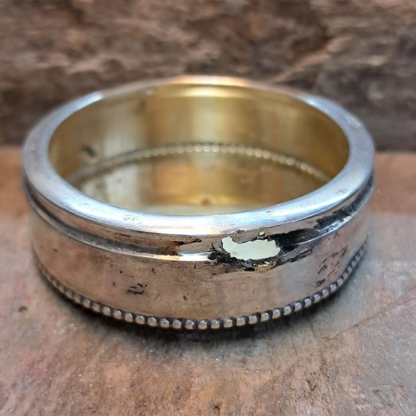 Ein Vintage-Silberring mit goldenem Innenraum, der Gebrauchsspuren aufweist, ruht auf einer rustikalen Holzoberfläche.
