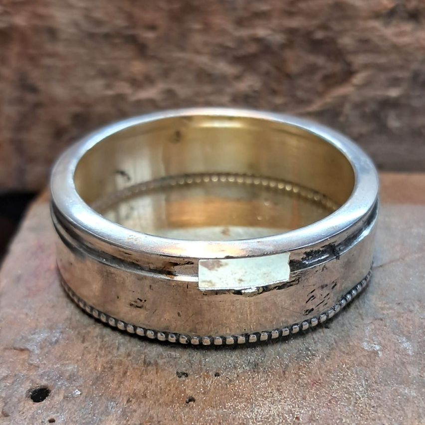 Ein Silberring mit strukturierter Band und einem kleinen Diamanteinsatz, der auf einer Holzoberfläche liegt.