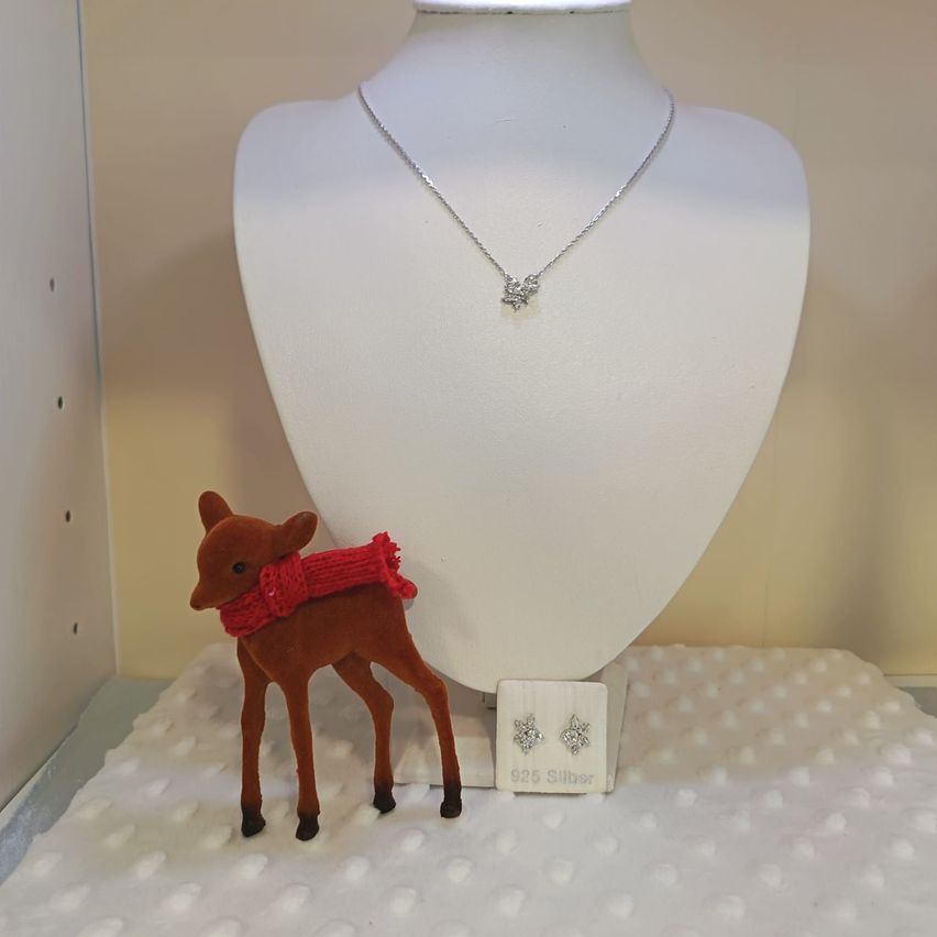Eine Halskette mit silbernem Anhänger und passende Ohrringe sind auf einem Mannequin ausgestellt, mit einer Rehenfigur in roter Schürze im Vordergrund.