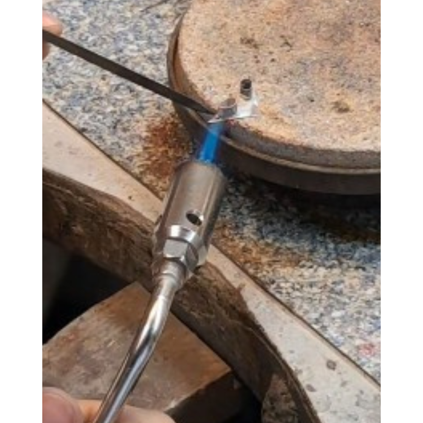 Eine Person erhitzt mit einer Fackel ein Metallteil auf einer Granitoberfläche mit einem Metallwerkzeug, das in ein Loch ragt.