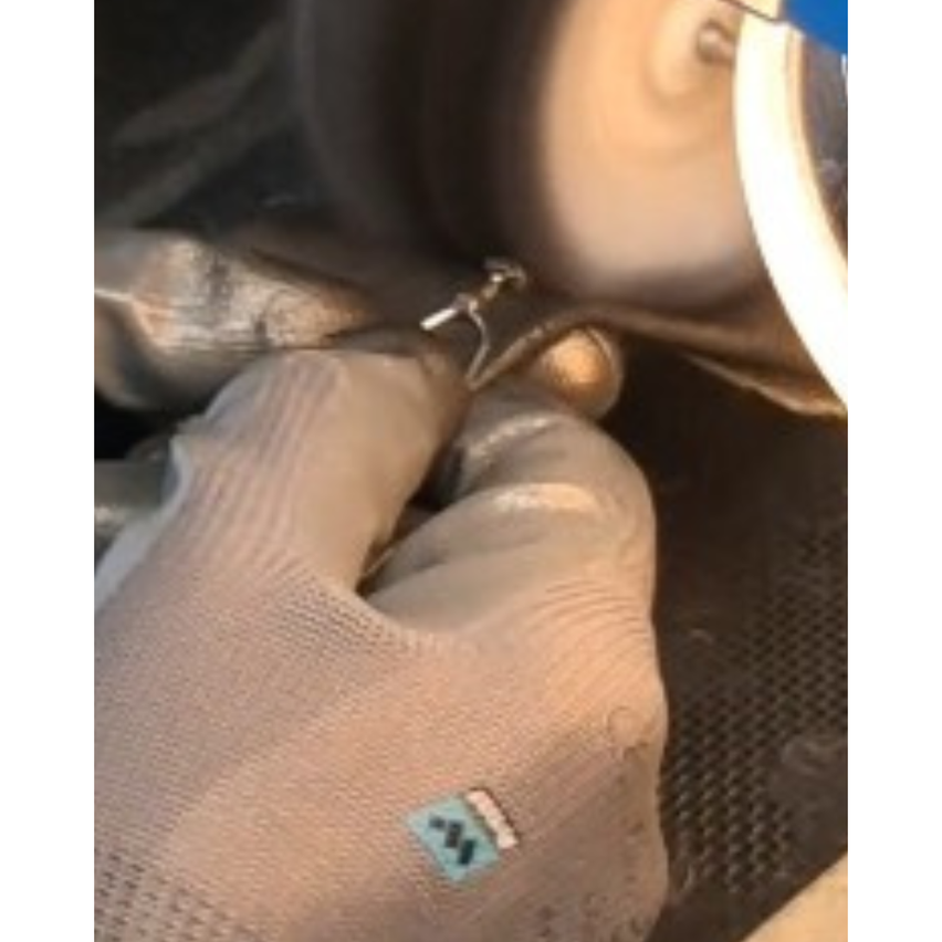 Eine behandschuhte Hand hält ein Metallobjekt in der Nähe eines sich drehenden Rades. Der Handschuh hat ein kleines Logo auf der Handfläche.