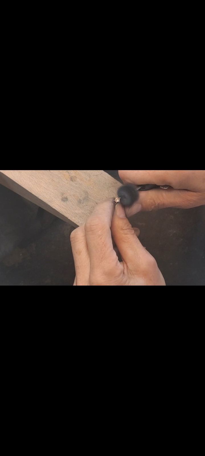 Eine Hand benutzt ein Werkzeug, um auf einer Holzoberfläche zu arbeiten. Ein Ring liegt auf dem Tisch.