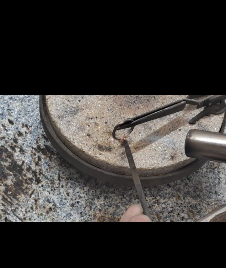 Eine Nahaufnahme eines Metallobjekts, das von einer Hand gehalten wird, möglicherweise ein Lötkolben. Das Objekt hat eine Metallspitze und ist mit einem Draht verbunden.